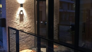 En modern byggnadsfasad med en glasdörr, ett metallräcke och en tegelvägg med en lampa.