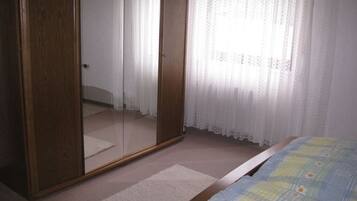 Ein Schlafzimmer mit Holzschrank, einem Bett mit Blumenmuster und durchscheinenden Vorhängen.