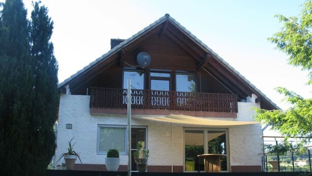 Una casa de dos pisos con un balcón, una antena parabólica y un ventanal grande.