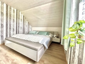 Une chambre avec un plafond en pente, un lit avec une tête de lit, une table de chevet et une plante en pot.