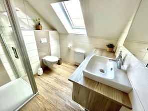 Un baño moderno con tragaluz, inodoro, lavamanos y ducha.