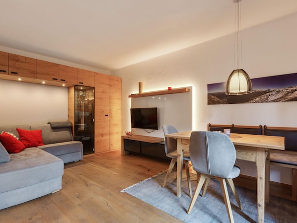 A modern living room with a grey sofa, wooden cabinets, and a dining area with a wooden table and chairs.