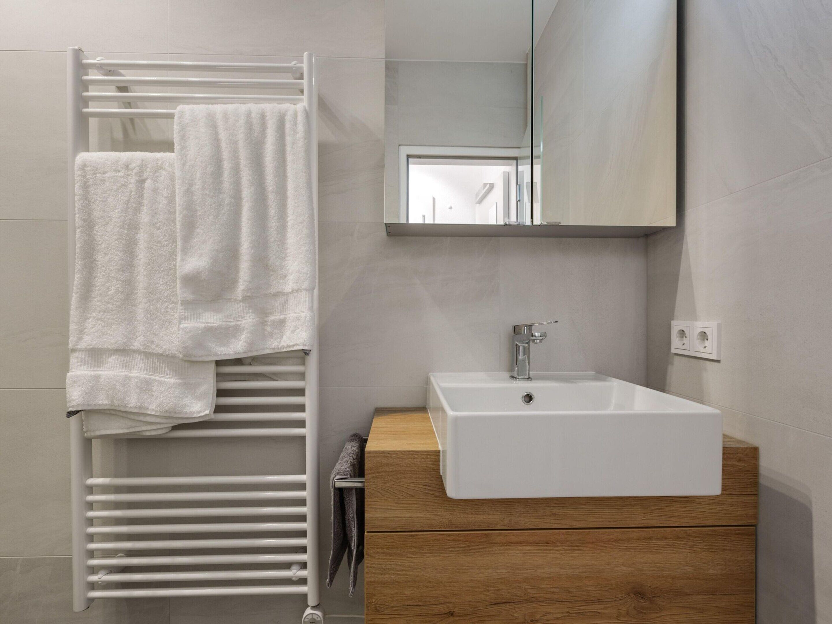 A bathroom with a white sink, wooden vanity, and a towel rack with a white towel.