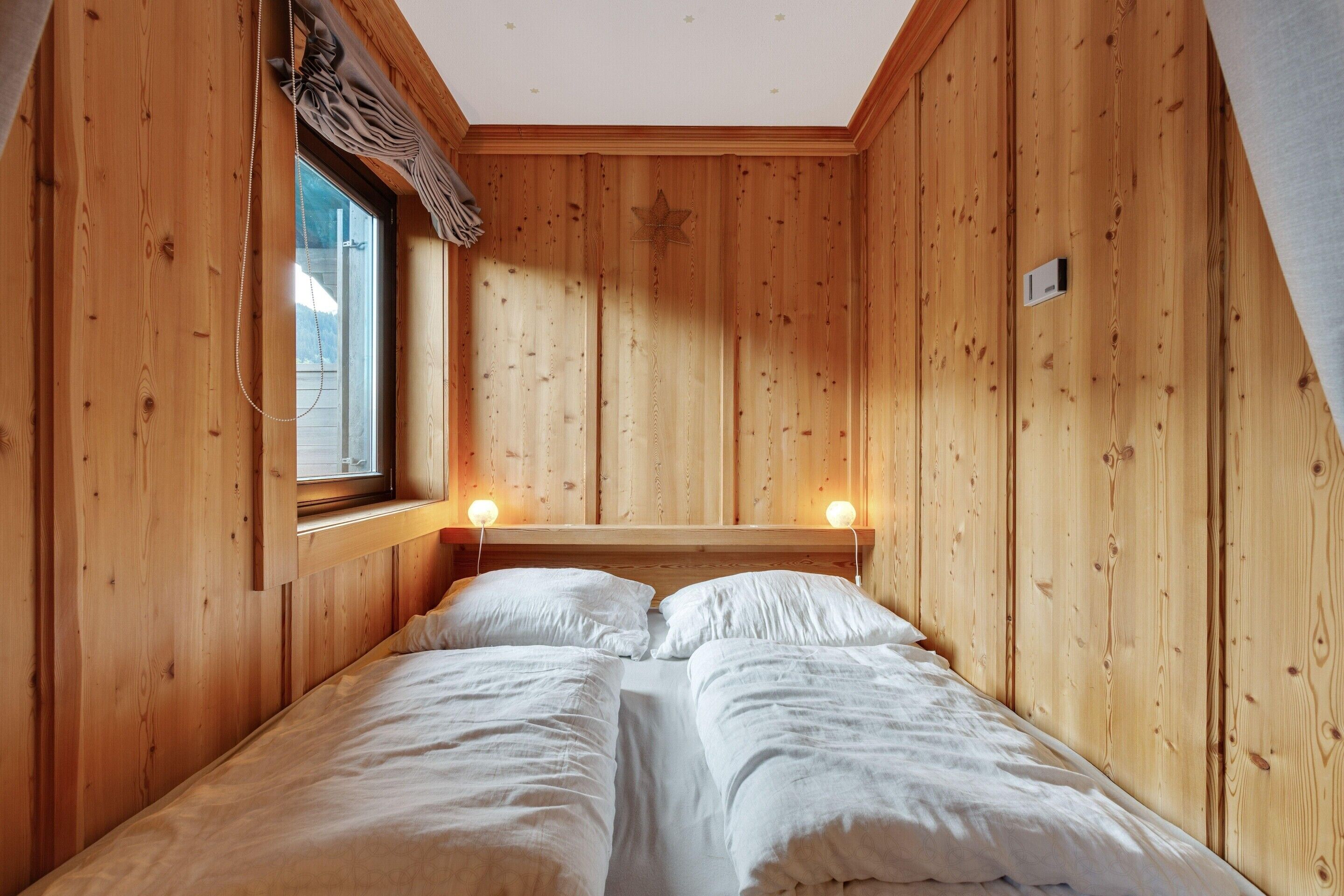 A wooden room with a bed, a window, and two wall-mounted lights.