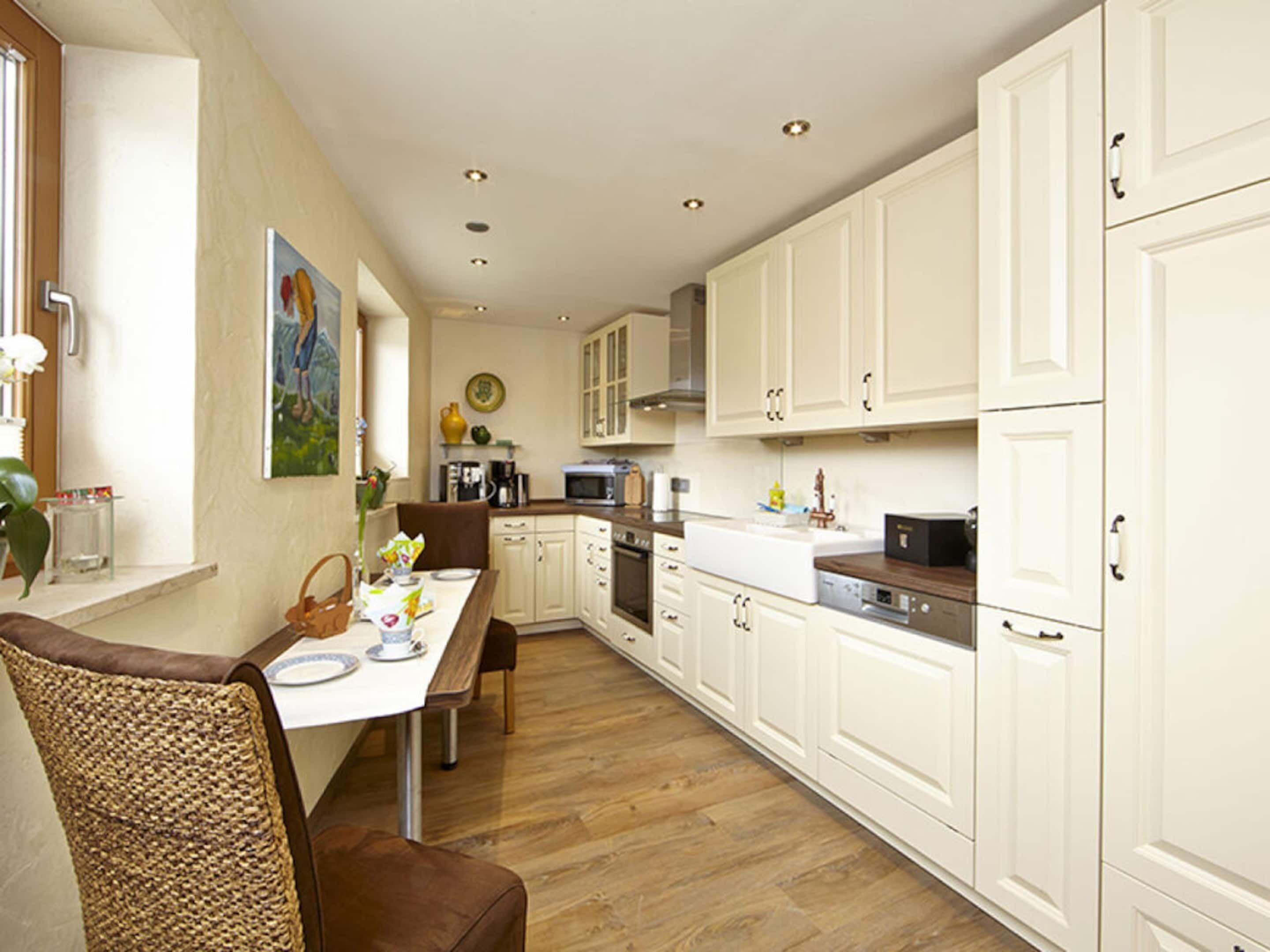 A modern kitchen with white cabinets, a dining table with chairs, and a painting on the wall.