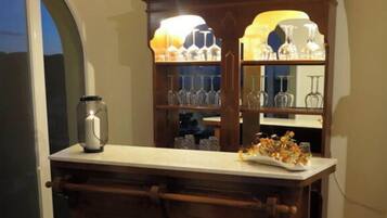 A bar area with a wooden bar counter, two stools, and a cabinet with glassware.