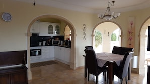 A dining area with a table and chairs, a kitchen with white cabinets, a ceiling fan, and a clock on the wall. - en la Montana Comfortable Holiday Residence (Pedreguer)
