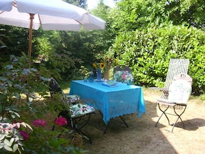 Relax in a serene outdoor setting with a table for two, a vase of sunflowers, and a comfortable chair with a floral cushion.