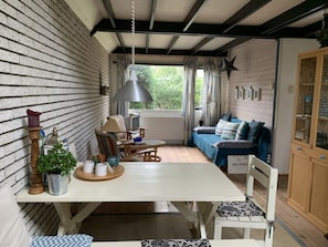 Relax in this charming room with a wooden dining table, comfortable armchair, and sofa, surrounded by exposed beams and a brick-patterned wall.