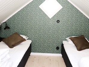 Quarto com duas camas, uma janela e parede com papel de parede estampado.