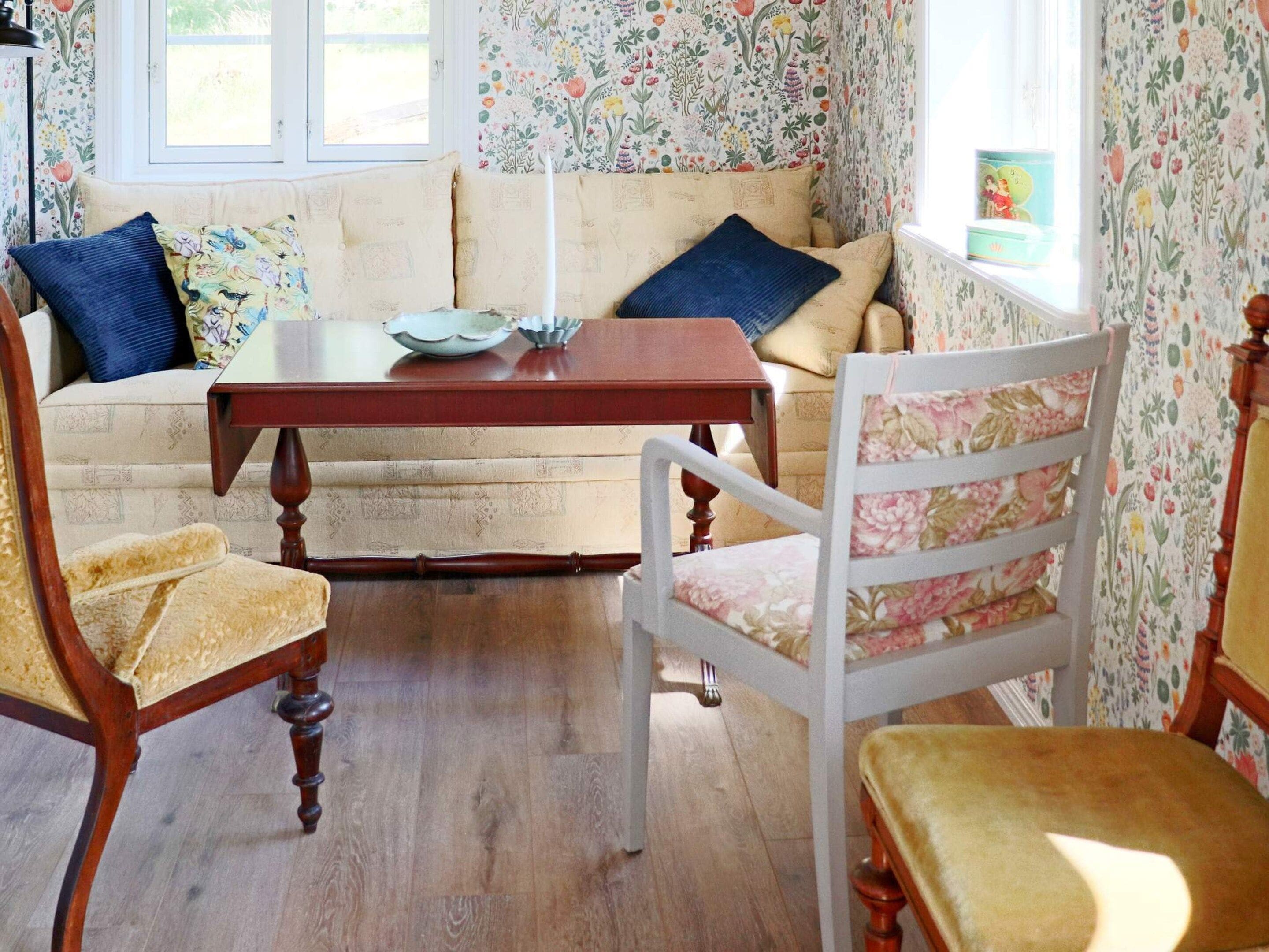 A cozy room with a sofa, two chairs, a wooden table, and floral wallpaper.