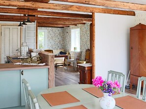 Una cocina rústica con vigas de madera, una mesa de comedor con sillas y un cuarto de fondo con papel tapiz floral.