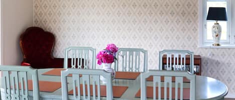A dining area with a table and chairs, a decorative vase with flowers, and a window with a lamp.