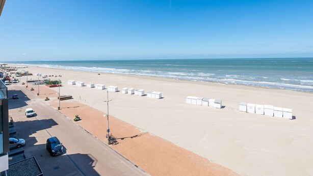 Une vue sur la plage avec un espace de stationnement, une rangée de chaises de plage blanches et un ciel bleu dégagé.