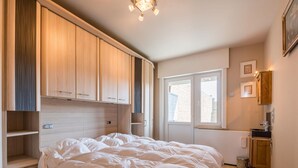Une chambre dotée d’un grand lit, d’une armoire en bois intégrée et d’une fenêtre laissant entrer la lumière naturelle.