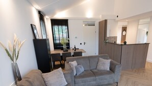 Ein modernes Wohnzimmer mit einer grauen Sofagarnitur, einem Holztisch und einem Essbereich mit Holztisch und Stühlen.