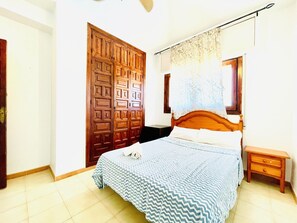 A bedroom with a wooden bed, a nightstand, a wooden wardrobe, and a window with a curtain. - Mountain-view Apartment by Sea (Roquetas de Mar)