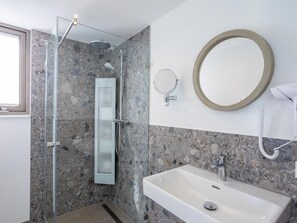 Un baño moderno con ducha de mampara de vidrio, un espejo rectangular, un espejo redondo y un lavamanos blanco.