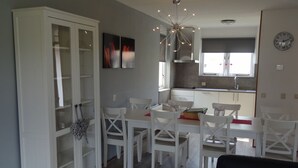 Une cuisine moderne avec des meubles blancs, un coin repas avec des chaises blanches et un canapé noir.