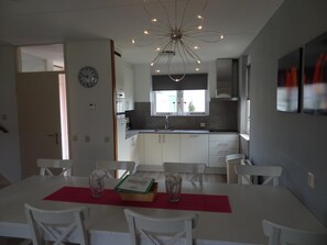 Cozinha moderna com armários brancos, uma ilha central e uma área de jantar com mesa e cadeiras brancas.