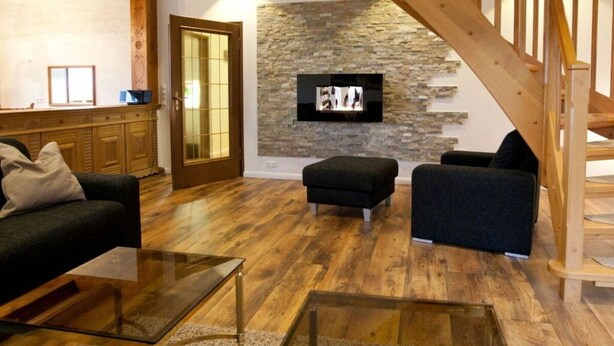 A living room with a stone wall, wooden floor, and a staircase. - Habel Modern Retreat (Nebel)