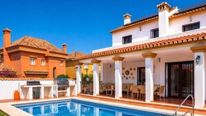 A swimming pool with a patio area, outdoor furniture, and a barbecue setup.