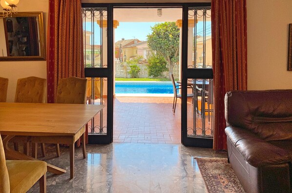 A room with a dining table, chairs, a sofa, and a view of a swimming pool and greenery outside. - Ref: 325 Villa Elena - Large villa with private Pool (Fuengirola)