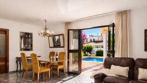 A living room with a dining area, a sofa, a coffee table, and a view of a pool and garden.