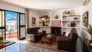 A living room with a fireplace, two sofas, a coffee table, and a balcony with a chair.