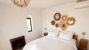 A bedroom with a large bed, two bedside tables, a wall-mounted lamp, a mirror, and a small window.