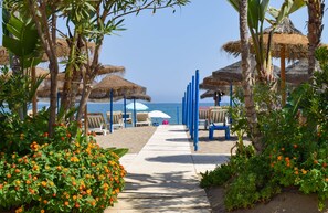 A pathway leading to beach umbrellas and lounge chairs, surrounded by tropical plants and palm trees. - Ref: 325 Villa Elena - Large villa with private Pool (Fuengirola)