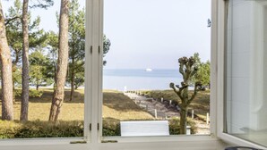 A room with a large window overlooking a coastal landscape with trees and a distant view of the sea. - Sea Lymphony - in Villa Frigga (Binz)