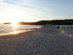 Une plage avec un ciel dégagé, un coucher de soleil et quelques personnes qui se promènent.