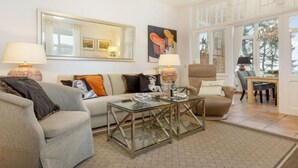 A living room with a sofa, armchairs, a glass coffee table, and a dining area with a table and chairs. - Sea Lymphony - in Villa Frigga (Binz)