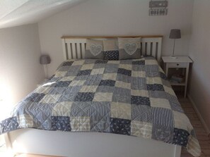 A bedroom with a quilted bedspread, a wooden headboard, two bedside lamps, and a nightstand with a lamp. - Holiday Apartment Inselstern (Fehmarn)