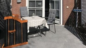 A brick house with a white-framed window, a door, and a small patio area with a table and chairs. - Holiday Apartment Inselstern (Fehmarn)