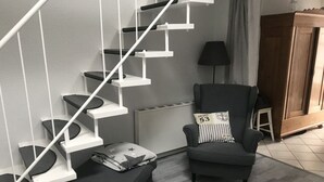 A modern living room with a white staircase, a black armchair with a striped pillow, a small ottoman, and a radiator. - Holiday Apartment Inselstern (Fehmarn)
