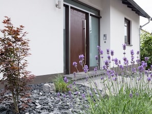 A modern house with a white exterior, a wooden door, and a small garden with purple flowers and a tree. - in the Moselschiefer House (Bernkastel-Kues)