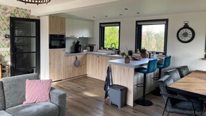 Eine moderne Küche mit Holzschränken, einem schwarzen Kühlschrank und einem Essbereich mit Holztisch und -stühlen.