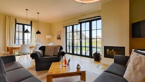 A spacious living room with a large window, a fireplace, and a flat-screen TV mounted on the wall. - Thatched Villa With Sauna and Fireplace (Dranske)