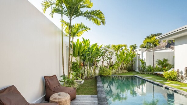 Ein moderner Poolbereich im Freien mit einer Holzterrasse, Liegestühlen und üppigen tropischen Pflanzen.