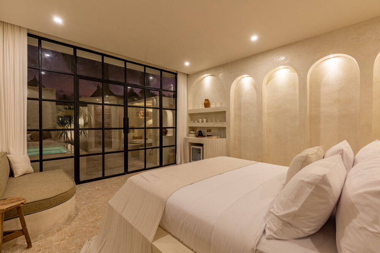 Un dormitorio amplio con una cama grande, una zona de estar y vistas a una zona de piscina a través de un ventanal.