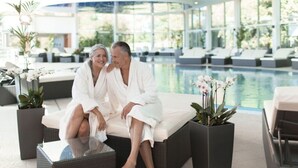 A couple sitting on a white sofa by a poolside, with a modern ceiling and lounge chairs in the background. - Holiday Apartment Old Town Hall (Tauberbischofsheim)