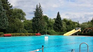 A swimming pool with a slide, surrounded by trees and a red bench. - Holiday Apartment Old Town Hall (Tauberbischofsheim)