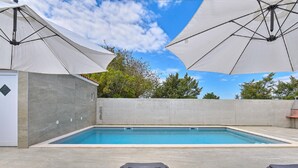 A swimming pool with two umbrellas, a concrete wall, and a door. - Modern Villa With Private Hydromassage Pool (Vodnjan)