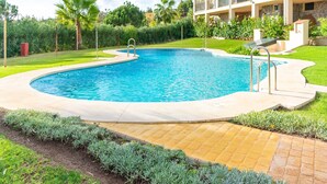 A swimming pool with a curved edge, surrounded by a paved deck and a grassy area with plants. - Belvilla by OYO Casa Roberto (Mijas)
