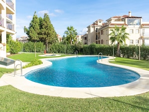 A swimming pool with a curved edge, surrounded by well-maintained grass and palm trees. - Belvilla by OYO Casa Roberto (Mijas)