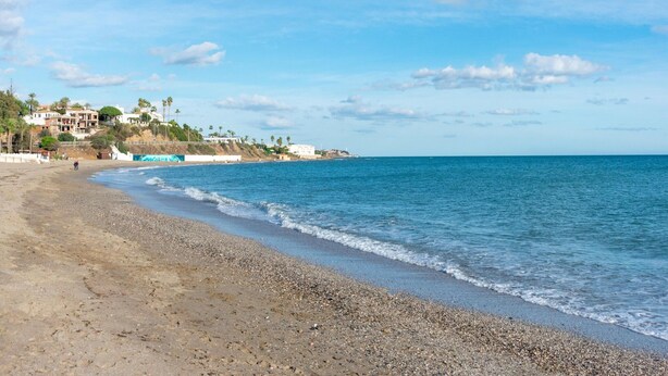 A beach with pebbly shore, calm sea, and buildings in the background. - Belvilla by OYO Casa Roberto (Mijas)