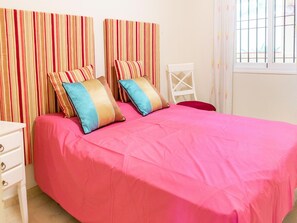 A bedroom with a bed, striped curtains, a white chair, and a window with bars. - Belvilla by OYO Casa Roberto (Mijas)