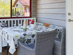Une table dressée avec une nappe à motifs floraux, une bouteille de jus de fruits, un vase rempli de fleurs et des chaises en osier.